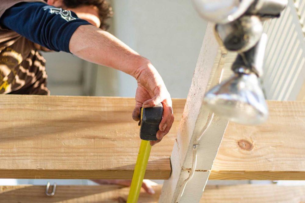 Ein Handwerker misst den Abstand zwischen zwei Brettern. (Totalunternehmer)